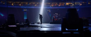 Movie still from “Metallica Through the Never” (2013), directed by Nimród Antal – A man standing on a stage with a microphone; Extreme Wide shot, High angle