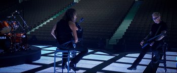 Movie still from “Metallica Through the Never” (2013), directed by Nimród Antal – A man sitting on a chair holding a cell phone; Wide shot, High angle