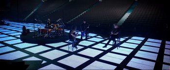 Movie still from “Metallica Through the Never” (2013), directed by Nimród Antal – A group of people sitting on chairs in a room; Extreme Wide shot, High angle