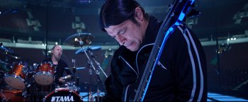 Movie still from “Metallica Through the Never” (2013), directed by Nimród Antal – A man playing a double bass in front of a drum set; Close Up shot, Low angle