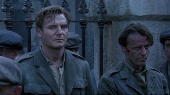 Movie still from “Michael Collins” (1996), directed by Neil Jordan – Two men in military uniforms standing next to each other near a fence; Close Up shot, Low angle