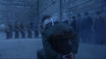 Movie still from “Michael Collins” (1996), directed by Neil Jordan – A group of people in a courtyard with a man in a military uniform and bandages on his head; Wide shot, Over the shoulder angle