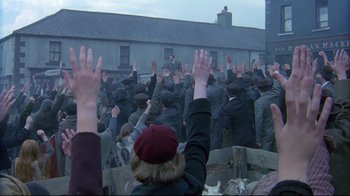 Movie still from “Michael Collins” (1996), directed by Neil Jordan – A group of people raising their hands in front of a building; Wide shot, High angle
