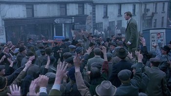 Movie still from “Michael Collins” (1996), directed by Neil Jordan – A crowd of people wearing hats and standing in front of a building; Wide shot, High angle