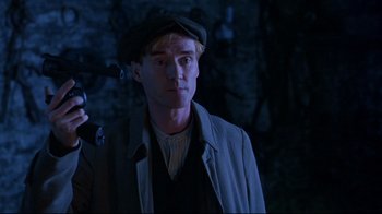 Movie still from “Michael Collins” (1996), directed by Neil Jordan – A man in a hat and a jacket looking to his left; Medium shot, Low angle