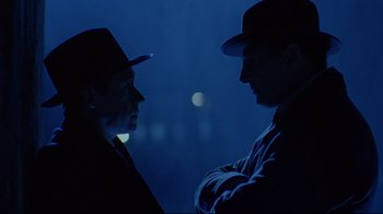 Movie still from “Michael Collins” (1996), directed by Neil Jordan – Two men in hats are talking in the dark; Close Up shot, Over the shoulder angle