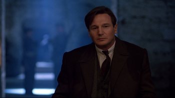 Movie still from “Michael Collins” (1996), directed by Neil Jordan – A man wearing a suit and tie standing in front of a building; Medium shot, Low angle