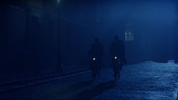 Movie still from “Michael Collins” (1996), directed by Neil Jordan – Two people riding bikes in the dark at night; Wide shot, Low angle