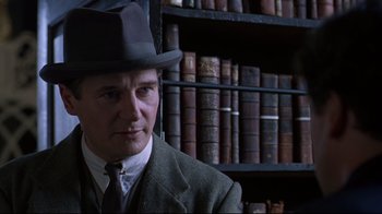 Movie still from “Michael Collins” (1996), directed by Neil Jordan – A man in a suit and hat in front of a book shelf; Close Up shot, Low angle