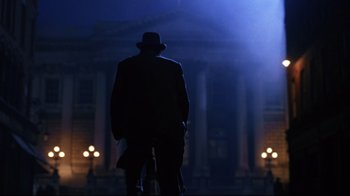 Movie still from “Michael Collins” (1996), directed by Neil Jordan – A man in a suit and a hat is riding a bike; Wide shot, Low angle