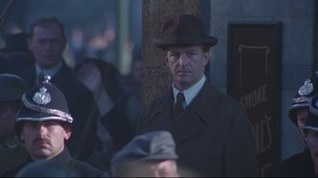 Movie still from “Michael Collins” (1996), directed by Neil Jordan – A man wearing a hat and a suit; Medium shot, Over the shoulder angle