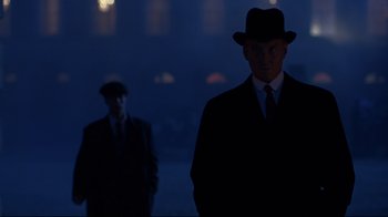 Movie still from “Michael Collins” (1996), directed by Neil Jordan – A man in a suit and hat standing in front of another man in a suit; Medium shot, Low angle