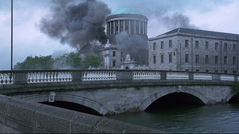 Movie still from “Michael Collins” (1996), directed by Neil Jordan – Smoke billows from a building on fire in a city; Extreme Wide shot, Low angle