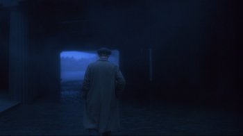 Movie still from “Michael Collins” (1996), directed by Neil Jordan – A man wearing a coat and hat is standing in the dark; Wide shot, Over the shoulder angle