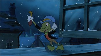 Movie still from “Mickey's Christmas Carol” (1983), directed by Burny Mattinson – A cartoon of jiminy cricket holding a paintbrush in the snow; Medium shot, Low angle