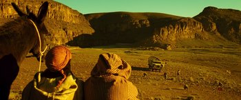 Movie still from “Micmacs” (2009), directed by Jean-Pierre Jeunet – A man standing on a dirt field near a jeep; Extreme Wide shot, Low angle