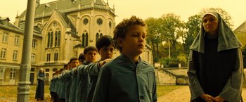 Movie still from “Micmacs” (2009), directed by Jean-Pierre Jeunet – A group of young men standing in front of a building; Medium shot, Low angle