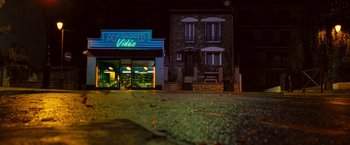 Movie still from “Micmacs” (2009), directed by Jean-Pierre Jeunet – A building with a neon sign in front of it at night; Extreme Wide shot, Low angle