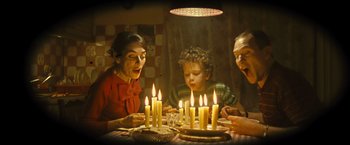 Movie still from “Micmacs” (2009), directed by Jean-Pierre Jeunet – A group of people sitting around a table with candles; Medium shot, High angle