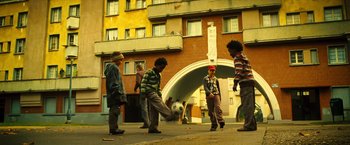 Movie still from “Micmacs” (2009), directed by Jean-Pierre Jeunet – A group of young boys playing soccer on a sidewalk; Wide shot, Low angle