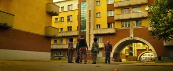 Movie still from “Micmacs” (2009), directed by Jean-Pierre Jeunet – A group of people standing in front of a tall building; Extreme Wide shot, Low angle