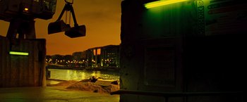 Movie still from “Micmacs” (2009), directed by Jean-Pierre Jeunet – A man laying on the ground next to a body of water at night; Extreme Wide shot, Low angle