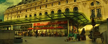 Movie still from “Micmacs” (2009), directed by Jean-Pierre Jeunet – People are sitting at tables outside of a restaurant; Extreme Wide shot, Low angle