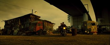 Movie still from “Micmacs” (2009), directed by Jean-Pierre Jeunet – Two people riding a motorcycle under a bridge; Wide shot, Low angle
