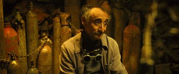 Movie still from “Micmacs” (2009), directed by Jean-Pierre Jeunet – An older man wearing goggles sitting in a room; Close Up shot, High angle