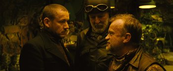 Movie still from “Micmacs” (2009), directed by Jean-Pierre Jeunet – A group of men standing next to each other in a room; Close Up shot, Over the shoulder angle