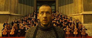 Movie still from “Micmacs” (2009), directed by Jean-Pierre Jeunet – A man standing in front of a group of people; Close Up shot, High angle