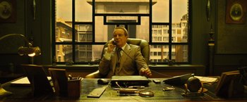 Movie still from “Micmacs” (2009), directed by Jean-Pierre Jeunet – A man sitting at a desk talking on a phone; Wide shot, Low angle