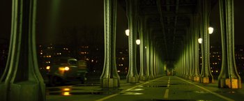 Movie still from “Micmacs” (2009), directed by Jean-Pierre Jeunet – A car driving down a street next to a bridge at night; Extreme Wide shot, Low angle