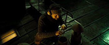Movie still from “Micmacs” (2009), directed by Jean-Pierre Jeunet – A man wearing headphones and a sweater is stirring something in a pot; Medium shot, High angle