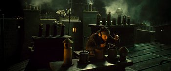 Movie still from “Micmacs” (2009), directed by Jean-Pierre Jeunet – A man is working in an industrial setting; Wide shot, Low angle