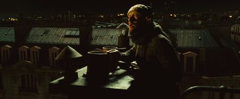 Movie still from “Micmacs” (2009), directed by Jean-Pierre Jeunet – A man sitting at a table drinking a cup of coffee; Medium shot, Low angle