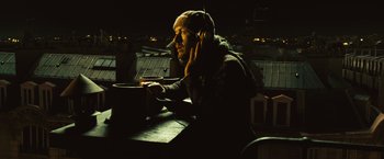 Movie still from “Micmacs” (2009), directed by Jean-Pierre Jeunet – A man sitting at a table in the dark listening to music; Medium shot, High angle