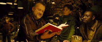 Movie still from “Micmacs” (2009), directed by Jean-Pierre Jeunet – An older man reading a book while a young boy looks on; Medium shot, High angle