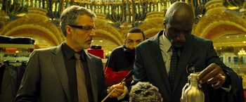 Movie still from “Micmacs” (2009), directed by Jean-Pierre Jeunet – A group of men standing around each other in front of a building; Medium shot, Low angle