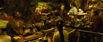 Movie still from “Micmacs” (2009), directed by Jean-Pierre Jeunet – A group of people sitting around a table with machines; Medium shot, High angle
