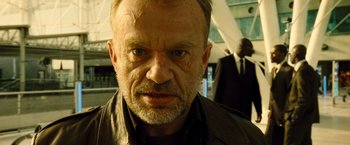 Movie still from “Micmacs” (2009), directed by Jean-Pierre Jeunet – An older man with a goatee stares into the camera; Close Up shot, Low angle