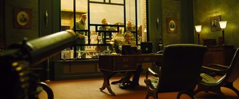 Movie still from “Micmacs” (2009), directed by Jean-Pierre Jeunet – A man sitting at a desk in front of a window; Wide shot, Over the shoulder angle