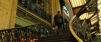Movie still from “Micmacs” (2009), directed by Jean-Pierre Jeunet – A man walking up a set of stairs in front of a building; Wide shot, Low angle