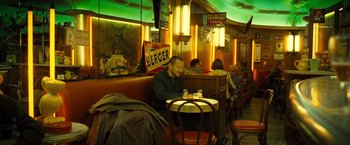 Movie still from “Micmacs” (2009), directed by Jean-Pierre Jeunet – A man sitting at a table in a restaurant; Wide shot, High angle