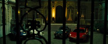 Movie still from “Micmacs” (2009), directed by Jean-Pierre Jeunet – A couple of cars parked in front of a building at night; Wide shot, High angle