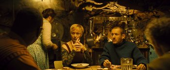 Movie still from “Micmacs” (2009), directed by Jean-Pierre Jeunet – Two people sitting at a table with a plate in front of them; Medium shot, Low angle