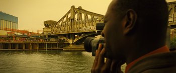 Movie still from “Micmacs” (2009), directed by Jean-Pierre Jeunet – A man taking a picture of a bridge with a camera; Medium shot, Low angle