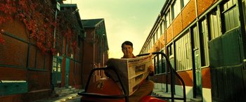 Movie still from “Micmacs” (2009), directed by Jean-Pierre Jeunet – A man sitting on a fire hydrant while reading a newspaper; Wide shot, Low angle