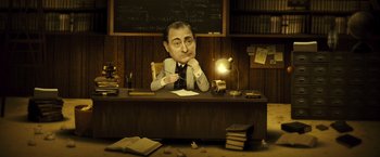 Movie still from “Micmacs” (2009), directed by Jean-Pierre Jeunet – A man sitting at a desk in front of a chalkboard; Medium shot, High angle