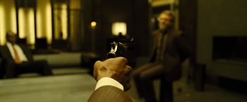 Movie still from “Micmacs” (2009), directed by Jean-Pierre Jeunet – A man holding a gun pointed at a man in a suit; Extreme Close Up shot, Over the shoulder angle